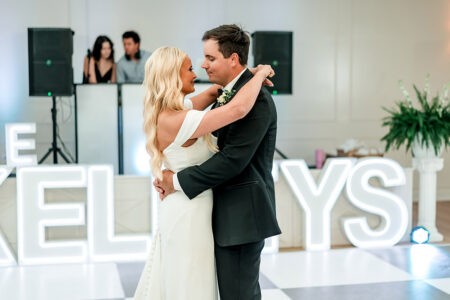 Bride and groom share their first dance at a New Orleans wedding on a checkered floor with KELLYS lights and DJ behind them.