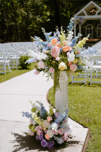 Colorful pastel floral arrangement on a white pedestal lining the outdoor ceremony aisle.