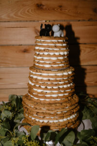 Three-tier chocolate chip cookie wedding cake with white frosting and black-and-white cat figurines on top.