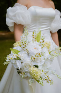 Close-up of the bride's white rose bouquet against her satin wedding gown with dramatic puff sleeves.